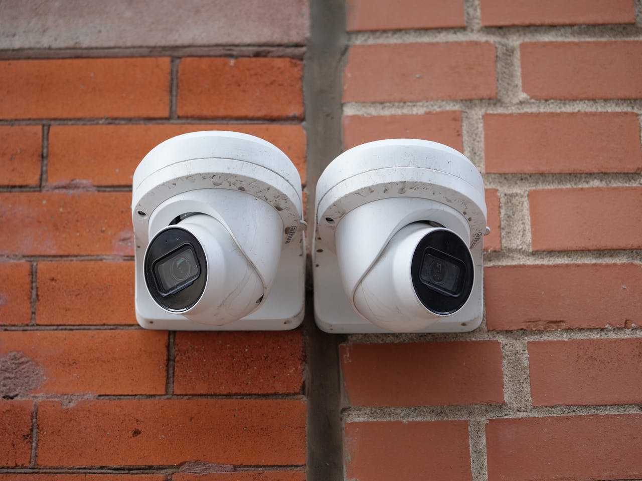 Mastering the First Impression: Your intriguing post title goes here Two white dome security cameras mounted on a brick wall for urban surveillance.